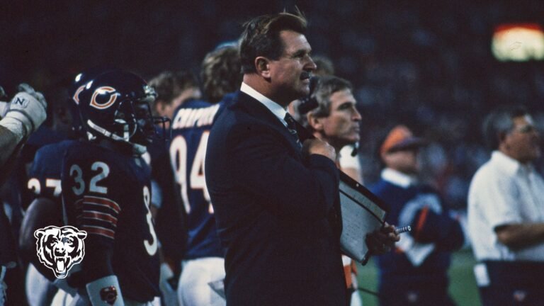 Mike Ditka watches a game from the Chicago Bears sideline beside players and coaching staff.