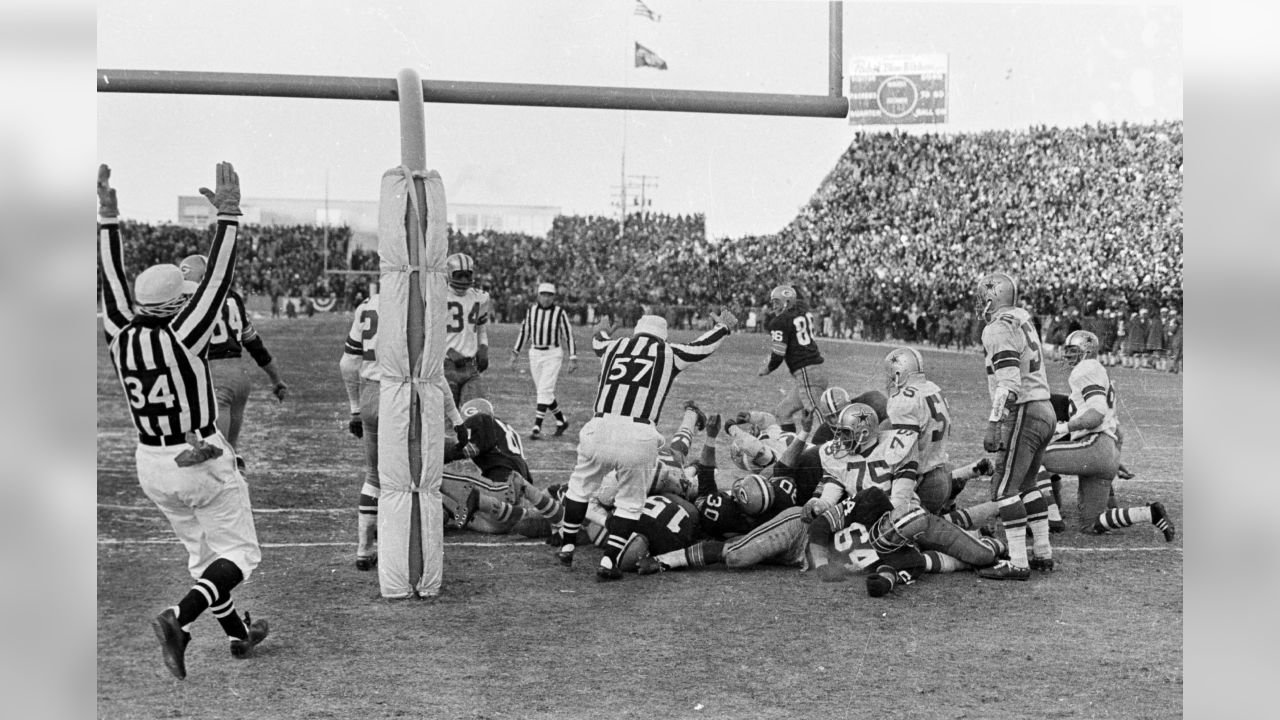 Officials raise their arms as Packers and Cowboys players lie in a pile at the Ice Bowl goal line.