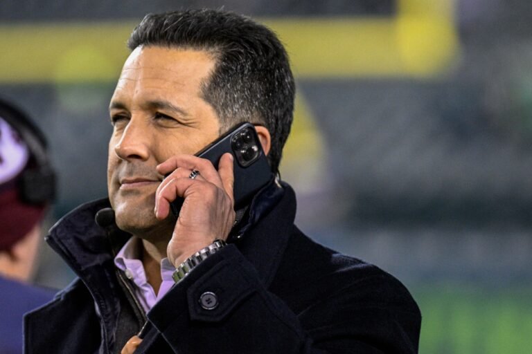 Adam Schefter speaking on a mobile phone on the sideline at Lincoln Financial Field in 2022.