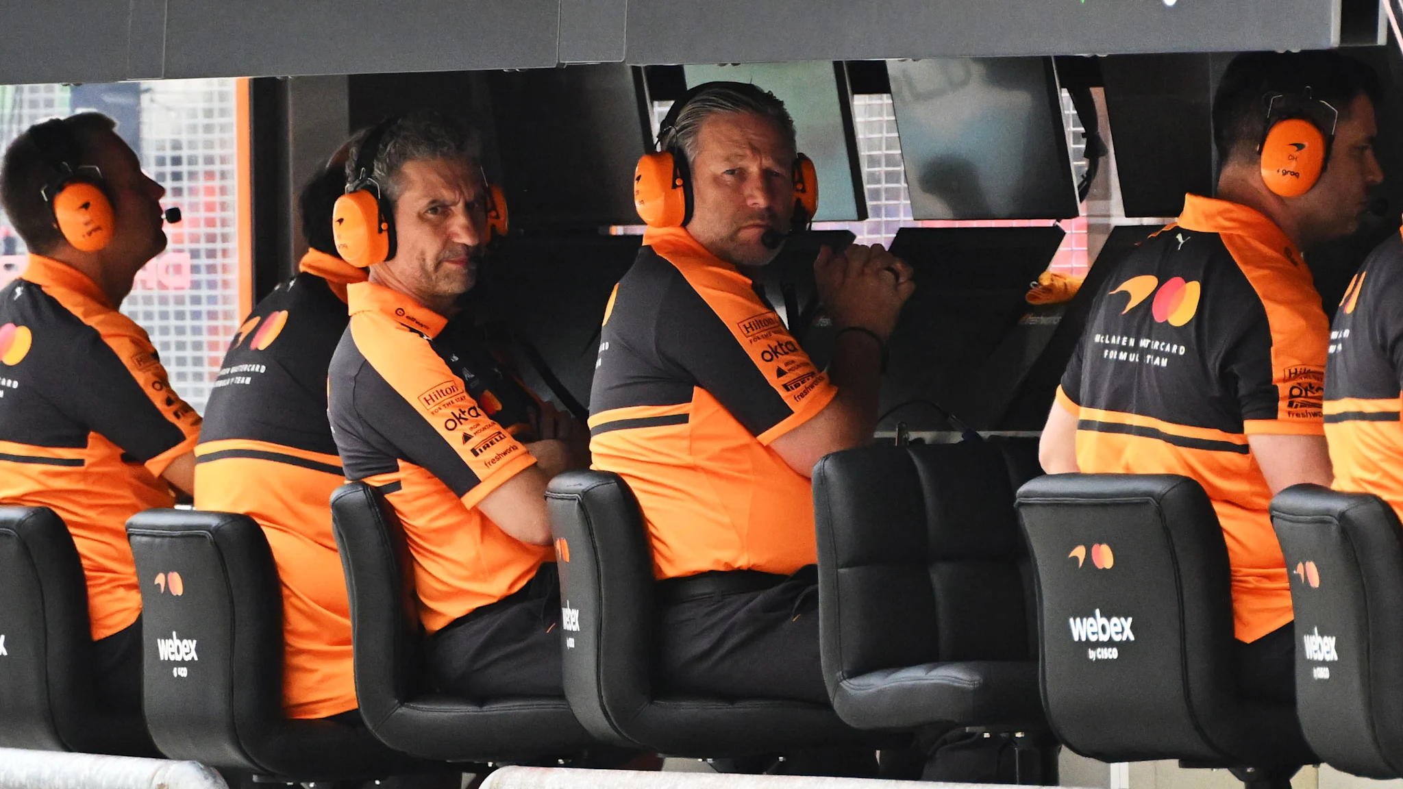 Andrea Stella and Zak Brown wear McLaren headsets on the pit wall.