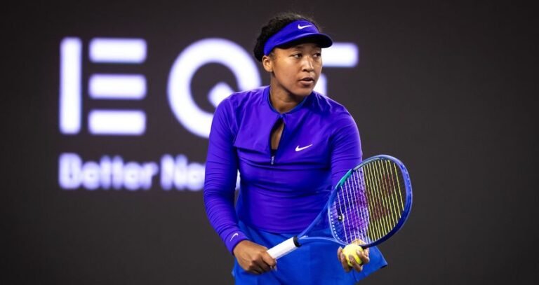 Naomi Osaka holds her racket and a tennis ball while wearing purple in Beijing.