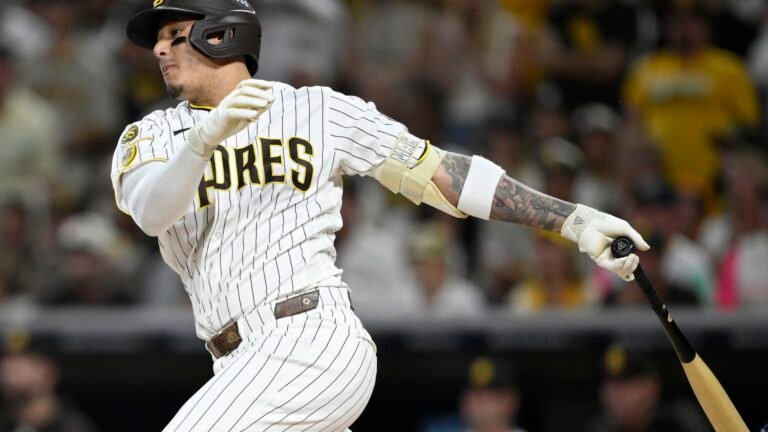 Manny Machado follows through with his bat in a white pinstriped Padres uniform at Petco Park.