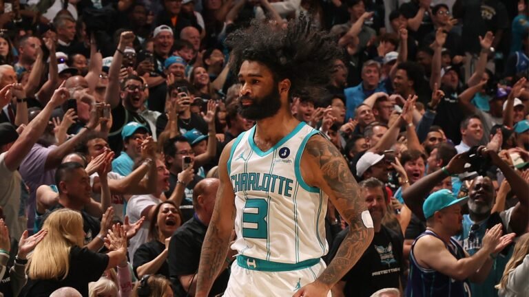 Coby White wearing a white Charlotte Hornets jersey with fans behind him.