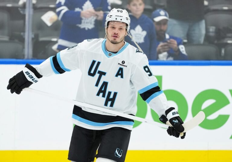 Mikhail Sergachev in a white Utah jersey holding his stick during warmups.