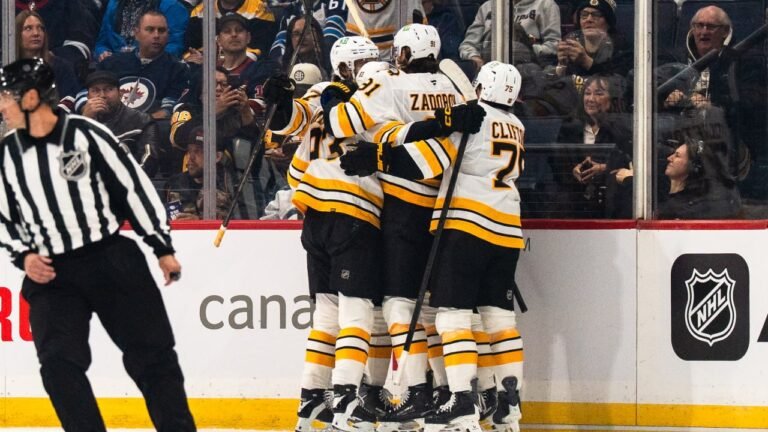 Bruins players in white road jerseys celebrate together beside the boards in Winnipeg.