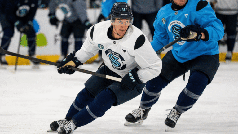 Mackie Samoskevich skates with the puck in a white Seattle Kraken training jersey and black No. 11 helmet.