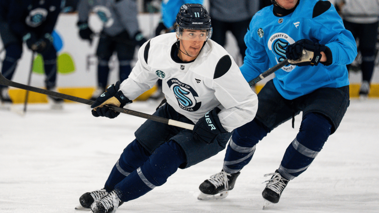 Mackie Samoskevich skates with the puck in a white Seattle Kraken training jersey and black No. 11 helmet.