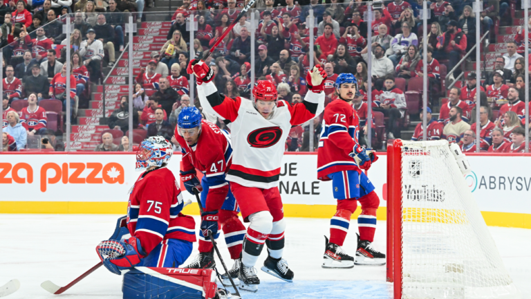 Taylor Hall raises his arms beside the Montreal net while wearing a white Carolina jersey.
