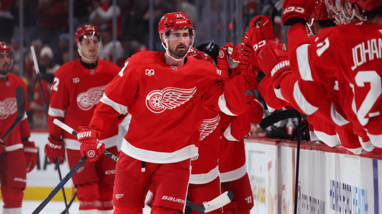 Dylan Larkin in a red Detroit jersey exchanges glove taps with teammates at the bench.