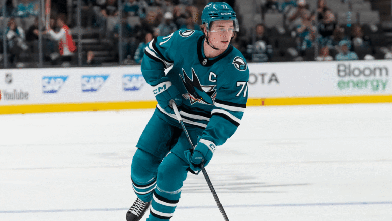 Macklin Celebrini skating in a teal San Jose Sharks jersey with his stick.