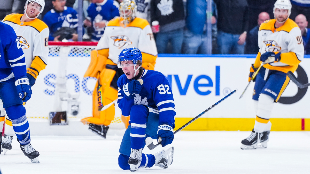 Gavin McKenna celebrates on one knee in a blue Toronto jersey with Nashville players behind him.