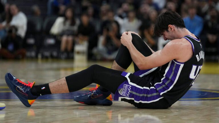 Maxime Raynaud holds his right knee while sitting on the court.