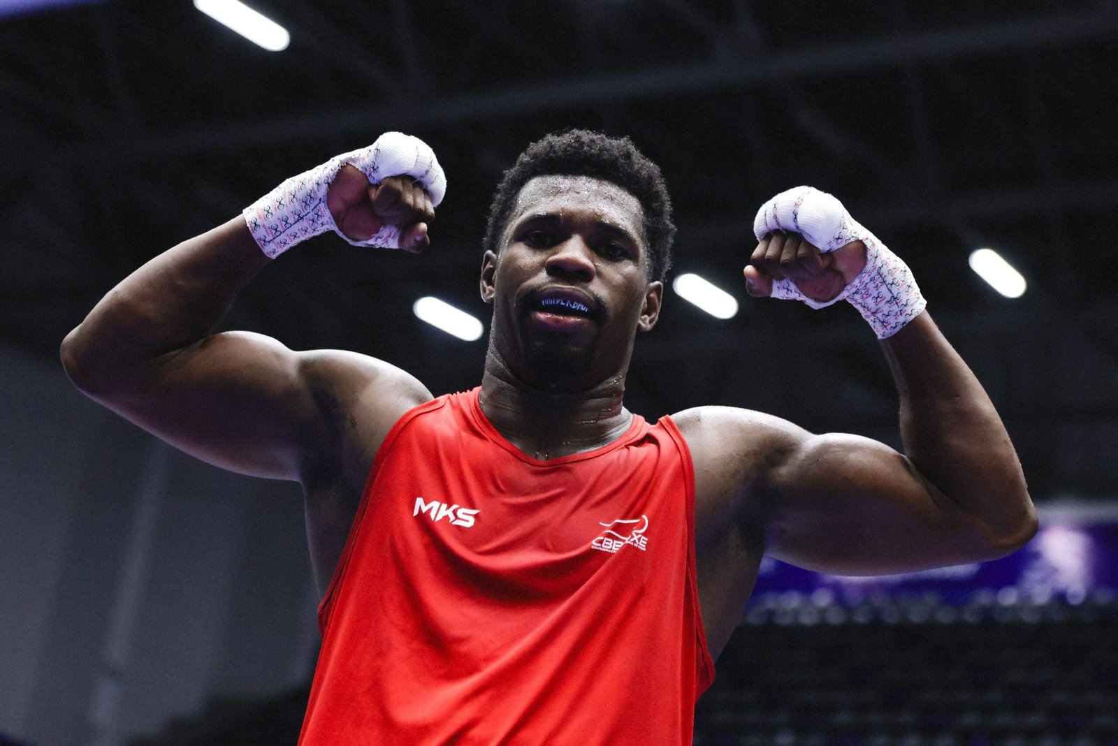 A boxer in a red vest raises both wrapped hands while posing at the Panamerican Championships