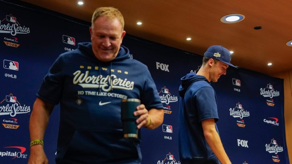 Brewers personnel in World Series clothing stand in front of the 2026 World Series media backdrop.