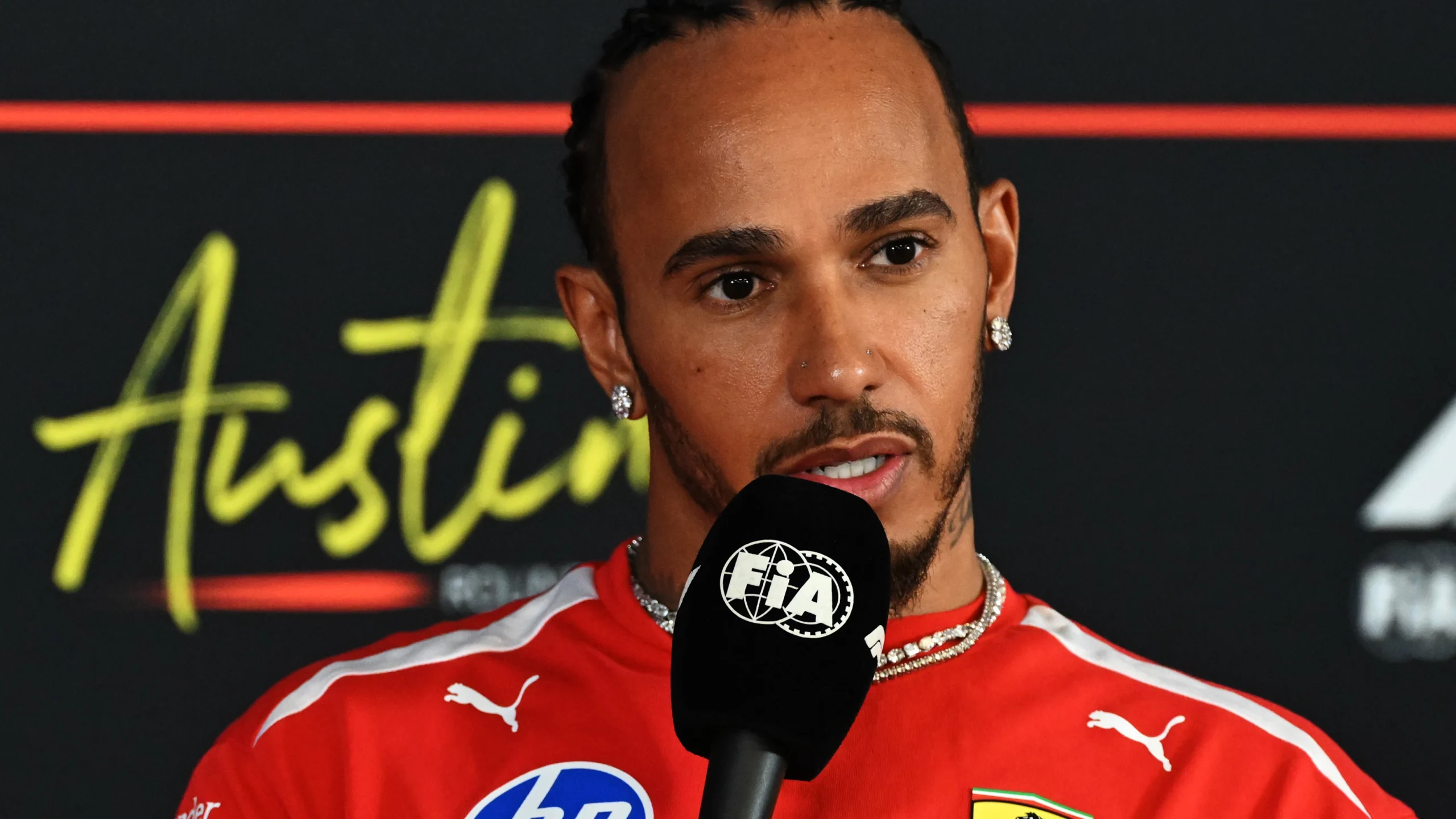 Lewis Hamilton in Ferrari team clothing speaks into an FIA microphone in Austin.