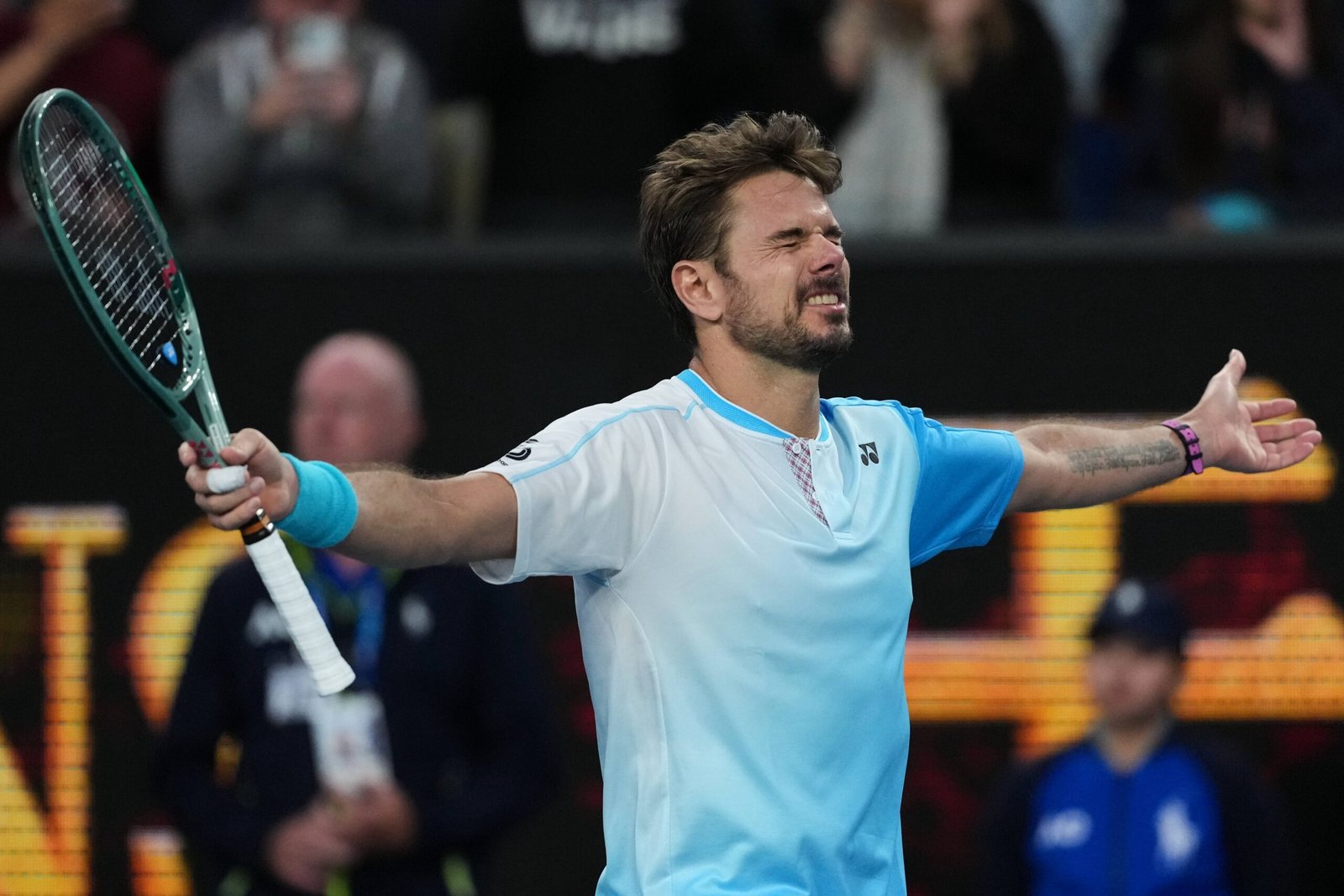 Stan Wawrinka spreads his arms in celebration on a blue tennis court.