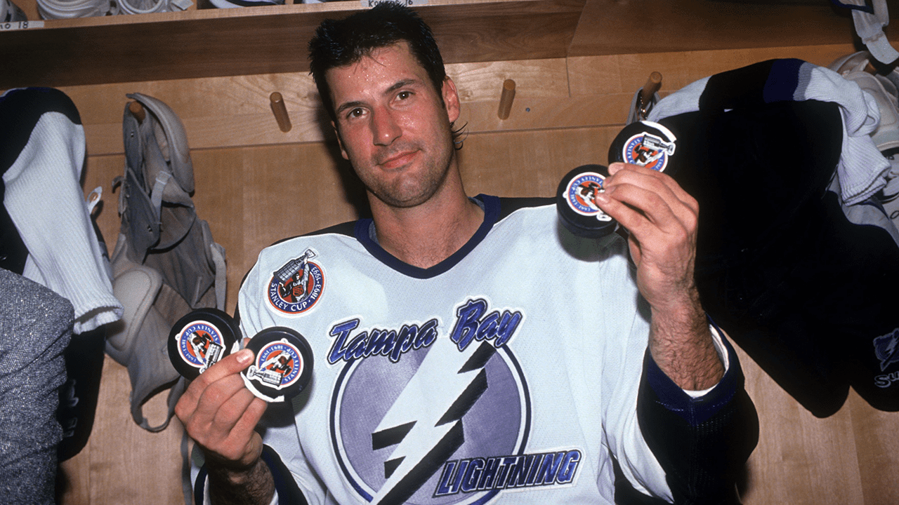 Chris Kontos holds four pucks while wearing a Tampa Bay Lightning jersey in an archival photograph.