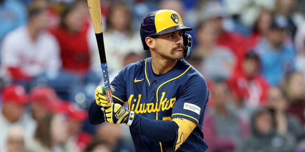 Joey Ortiz holds a bat while wearing a navy Brewers jersey and yellow batting helmet.