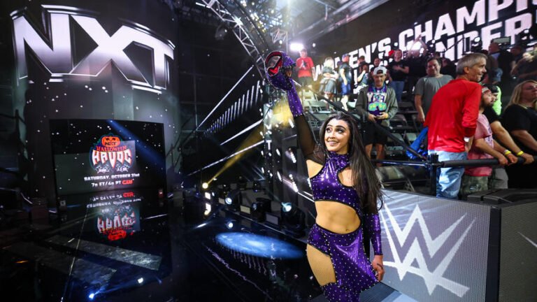A WWE NXT wrestler raises a championship belt on the entrance stage.