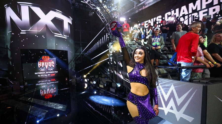 A WWE NXT wrestler raises a championship belt on the entrance stage.