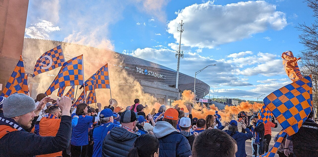 FC Cincinnati supporters wave flags and carry orange smoke on a stadium march