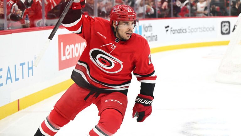 Logan Stankoven raises his stick in a red Carolina Hurricanes uniform