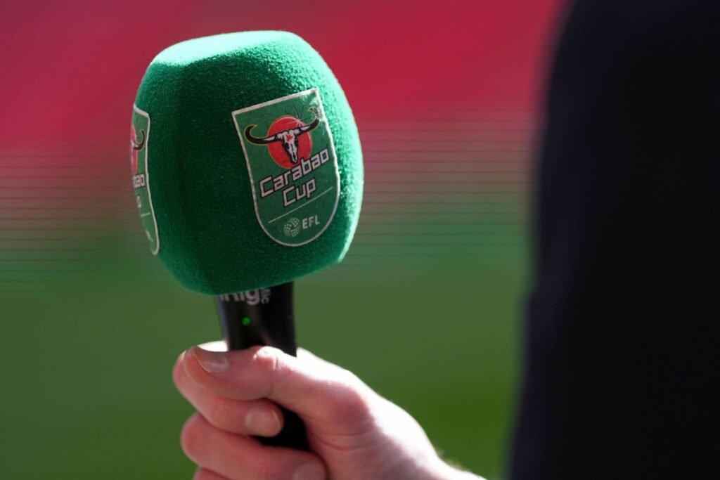 A green Carabao Cup microphone held beside a football pitch.